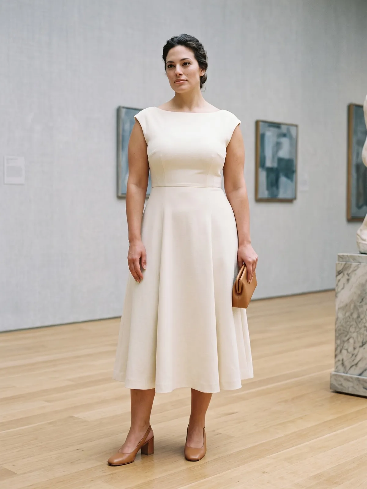 Frau mit Birnenfigur in einem cremefarbenen A-Linien-Midikleid mit anliegendem Oberteil und U-Boot-Ausschnitt, dazu hellbraune Slingback-Pumps