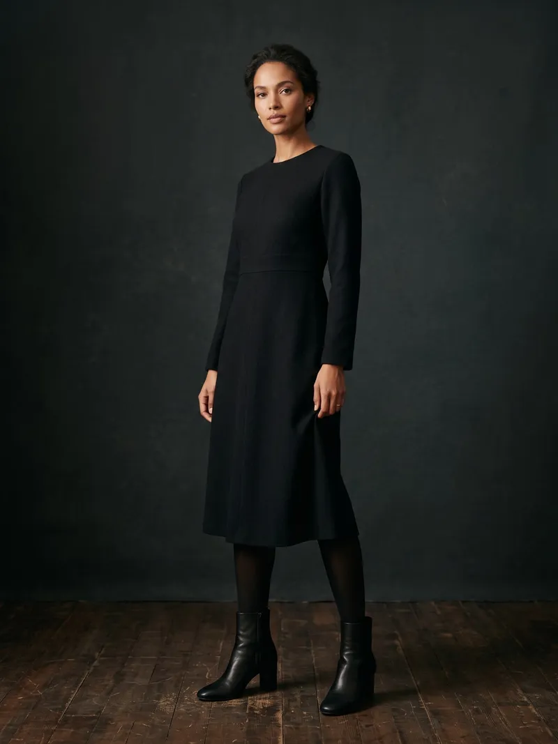 Frau in einem schwarzen Wollkleid mit blickdichter schwarzer Strumpfhose und schwarzen Stiefeletten vor dunklem Studiohintergrund